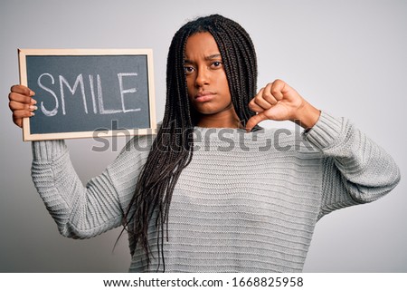 Young african american woman holding blackboard with smile word text over isolated background with angry face, negative sign showing dislike with thumbs down, rejection concept