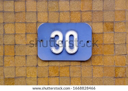 House Number 30 sign. Blue Number thirty plate mounted on a tiled wall.