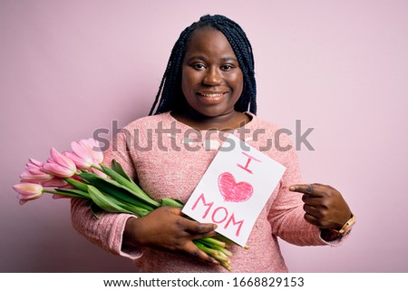 Plus size african american woman holding love mom message and tulips on mothers day very happy pointing with hand and finger