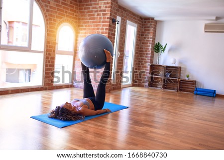 Middle age beautiful sportswoman doing exercise using fitness ball in a class of yoga at gym