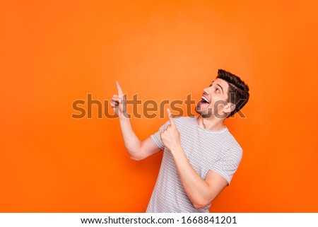 Photo of attractive funny crazy guy hold hands fingers direct up empty space excited good mood sales person wear striped t-shirt isolated bright orange color background