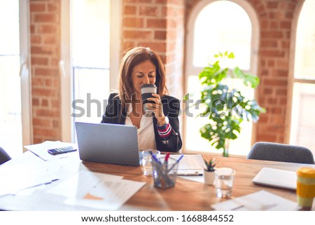 Middle age beautiful businesswoman smiling happy and confident. Sitting on chair working in a desk using laptop  drinking coffee at the office