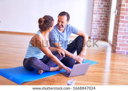 Middle age beautiful sporty couple smiling happy. Sitting on mat with smile on face using laptop at gym
