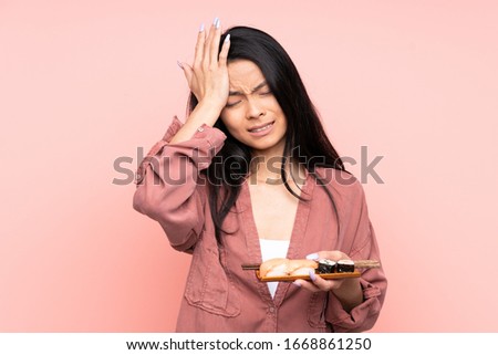 Teenager Asian girl eating sushi isolated on pink background having doubts with confuse face expression