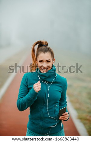 Young woman with ponytail is jogging in a park on foggy and cold day. Close photo of girl running outside on foggy day.