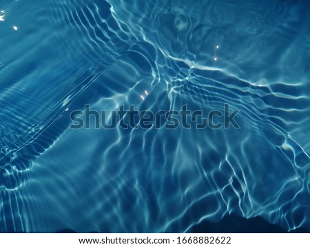 The​ pattern​ of surface​ blue​ water​ in​ the​ swimming​ pool reflected​ with sunlight​ for​ background. Abstract​ on surface​ blue​ water​ for​ background​