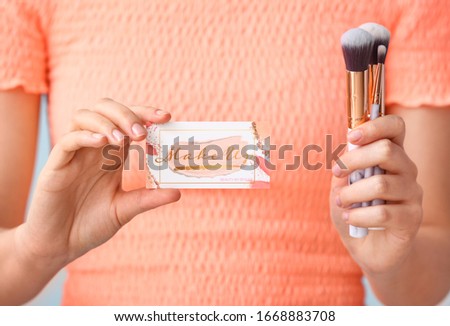 Woman with business card of makeup artist and brushes, closeup