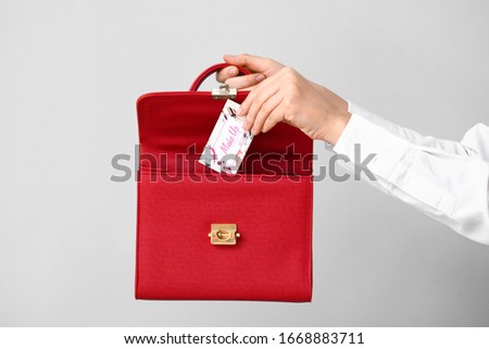 Female hands with business card of makeup artist and bag on grey background
