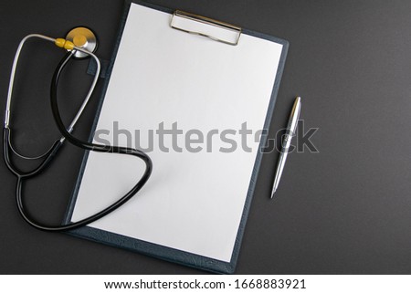 White sheet paper with silver pen, phonendoscope on black background with copy space for text. Medicine consept.