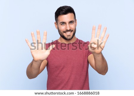 Young handsome man with beard over isolated blue background counting nine with fingers