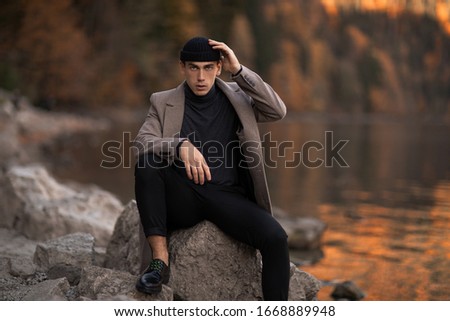 One male model dressed with a stylish coat and a fall cap outside.