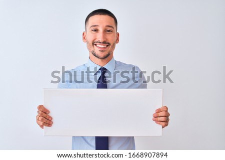 Young business man holding blank banner over isolated background with a happy face standing and smiling with a confident smile showing teeth