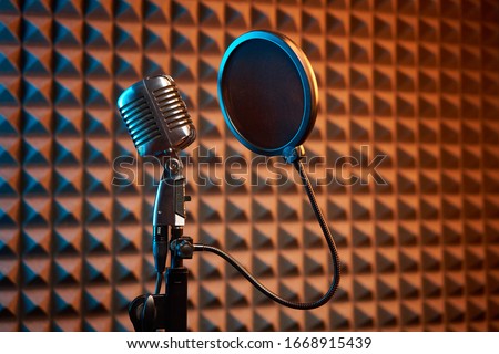 Retro microphone and pop filter for singing or recording a podcast on acoustic foam panel background, colorful light