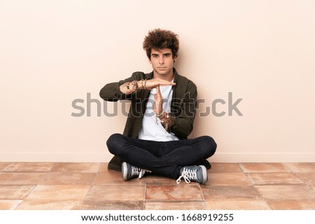 Young caucasian man sitting on the floor making time out gesture