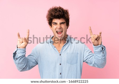 Young caucasian man with jean shirt over isolated pink background making rock gesture