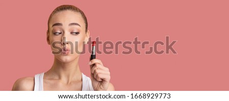 Makeup Concept. Young Woman Holding Lipstick Pouting Lips Standing On Pink Background In Studio. Panorama With Copy Space