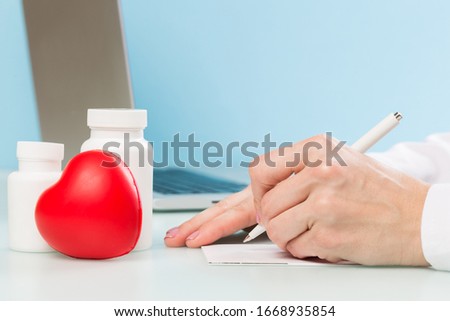 Doctor's hand uses a laptop and writes with a pen on paper on a blue background. medicine concept, modern technology