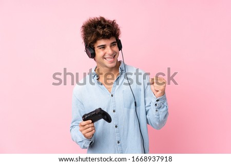 Young caucasian man over isolated pink background playing at videogames