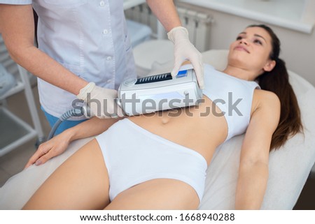 Enjoying ultrasound massage. Dark-haired woman wearing underwear lying and enjoying ultrasound massage