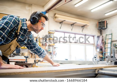 Carpenter using circular saw to cut a large wooden board at carpentry workshop Royalty-Free Stock Photo #1668966184