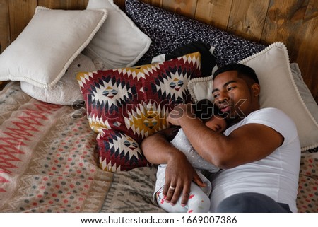 Kind young African American father calms his little mixed race crying two-year-old daughter lying on the bed in a cozy room. The concept of a caring father