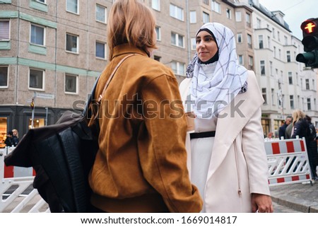 Young attractive Arabic woman in hijab talking with friend during walk around city 