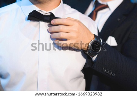 groomsman with watch helping groom with black bowtie Royalty-Free Stock Photo #1669023982