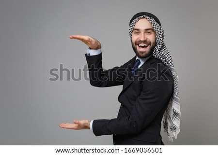 Arabian muslim businessman in keffiyeh kafiya ring igal agal classic black suit isolated on gray background. Achievement career wealth business. Gesturing demonstrating size with vertical workspace
