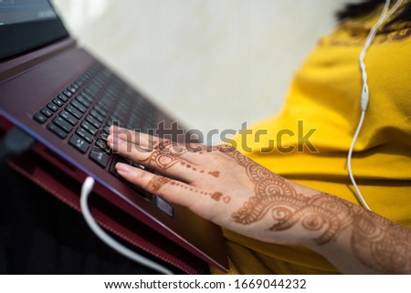 A young woman uses laptop keyboard and listen music with hand tatooed with henna design
