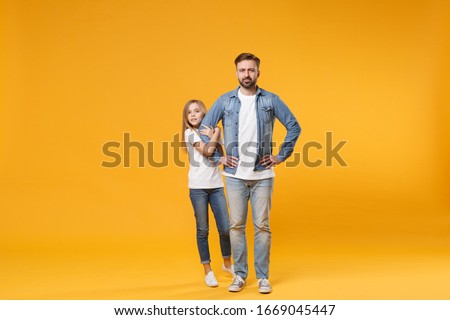 Bearded man in casual clothes with child baby girl. Father little kid daughter isolated on yellow background. Love family parenthood childhood concept. Stand with arms akimbo on waist holding hands