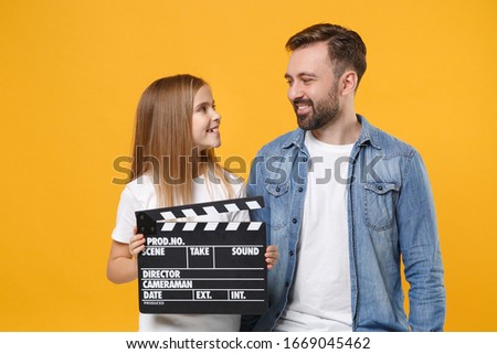 Smiling bearded man have fun with child baby girl. Father little kid daughter isolated on yellow background. Love family day parenthood childhood concept. Hold classic black film making clapperboard