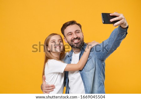 Bearded man in casual clothes with child baby girl. Father little kid daughter isolated on yellow background. Love family day parenthood childhood concept. Doing selfie shot on mobile phone, hugging