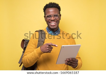 Happy african american college student holding tablet on isolated yellow background