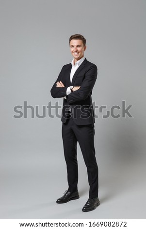 Successful young business man in classic black suit shirt posing isolated on grey wall background studio portrait. Achievement career wealth business concept. Mock up copy space. Hold hands crossed Royalty-Free Stock Photo #1669082872