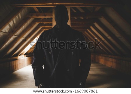 A scary guy in black mask and long dark coat standing in an abandoned attic. A man without a face. Scary and mystical picture. Horror concept.