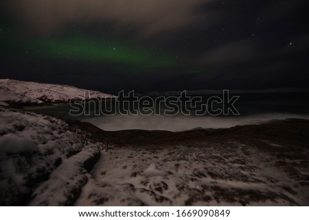 
aurora borealis in winter on the seashore with stones and rocks