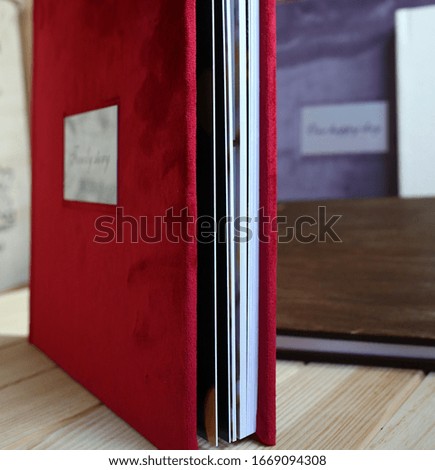 
album photo book with a metal insert and an inscription in a red villa cover with a decor next to flowers, 
side view
