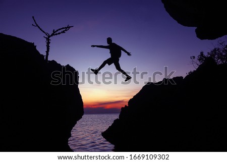 Silhouette of the photographer jumping over the stone at sunset ,Man Jumping between rocks on tropical Sea at twilight sky.