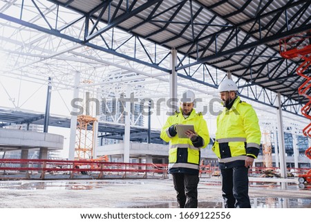 Men engineers standing outdoors on construction site, using tablet. Royalty-Free Stock Photo #1669122556
