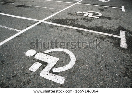 disabled bay marked with white stripes and special sign on grey wet asphalt at large parking lot on cloudy spring day closeup