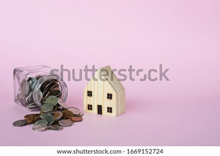 Wooden house model with money coins in the glass jar on pink background with copy space for business and finance for property concept