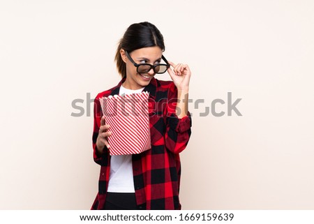 Woman over isolated background with 3d glasses and holding a big bucket of popcorns