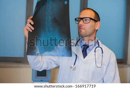 Male doctor in uniform looking at the x-ray picture of spinal column in hospital