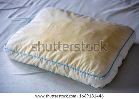 Old dirty used yellow sweat stained pillow on a mattress. Condition of the pillow used for a long time. 