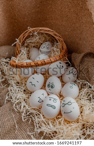Eggs with painted faces in a basket. A lot of eggs is near basket