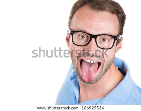 Closeup portrait of nerdy guy with big black glasses and blue shirt sticking tongue out at you camera gesture, isolated on white background. Negative emotion facial expression feelings.