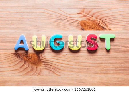 August word written with colorful letters on wooden background, top view