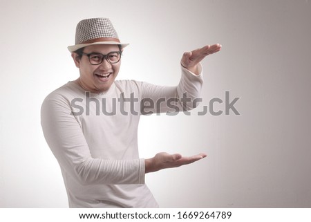Portrait of happy young Asian man showing something between his hands, copy space template over white background