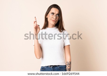 Young woman over isolated beige background with fingers crossing and wishing the best