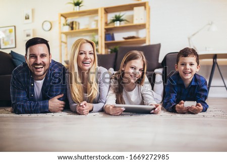 Young family of four relaxing on floor in living-room and watching movie or cartoons in digital tablet on weekend
